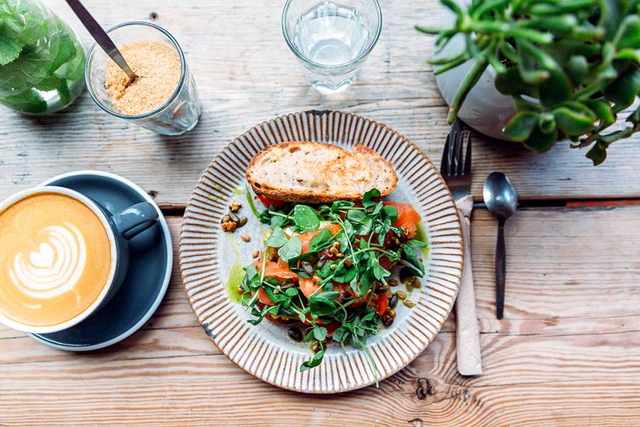 En smörgås med sallad på en tallrik med en kaffe latte i en kopp